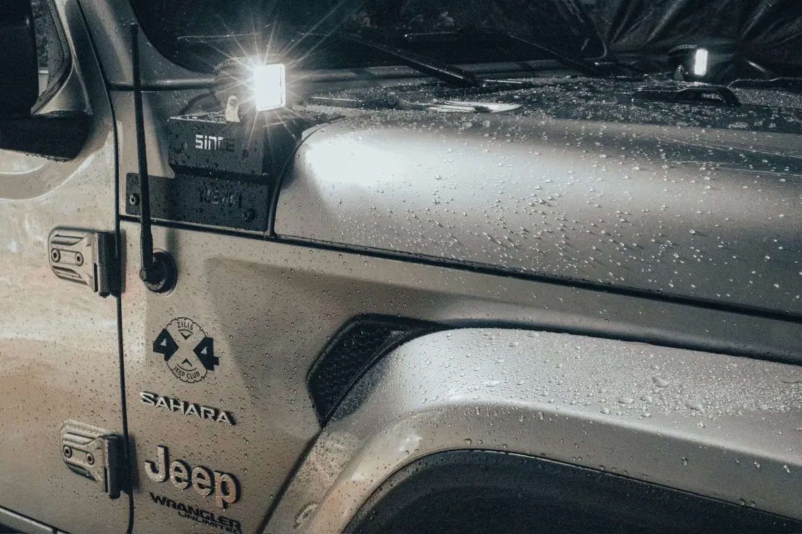 A jeep is parked in the rain with its hood open.